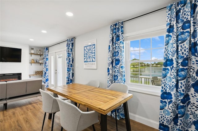 dining room featuring a large fireplace, a water view, wood-type flooring, and plenty of natural light