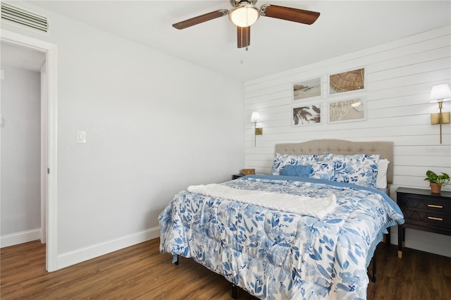 bedroom featuring ceiling fan, wooden walls, and dark wood-type flooring