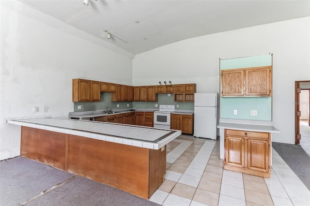 kitchen with sink, white appliances, light tile patterned floors, tile counters, and kitchen peninsula