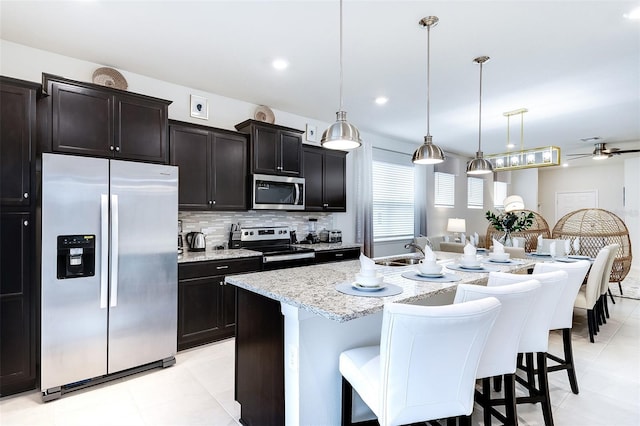 kitchen featuring an island with sink, appliances with stainless steel finishes, a kitchen bar, and decorative light fixtures