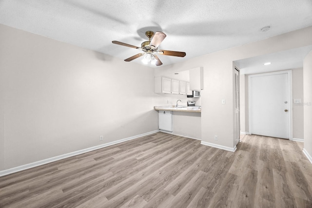 unfurnished living room featuring ceiling fan, sink, a textured ceiling, and light hardwood / wood-style floors