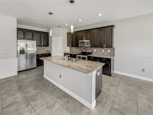 kitchen featuring a center island with sink, sink, hanging light fixtures, light stone countertops, and stainless steel appliances