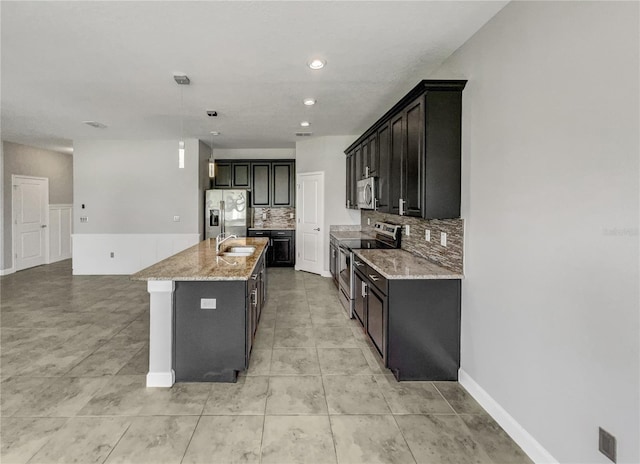 kitchen with light stone countertops, stainless steel appliances, tasteful backsplash, decorative light fixtures, and a center island with sink