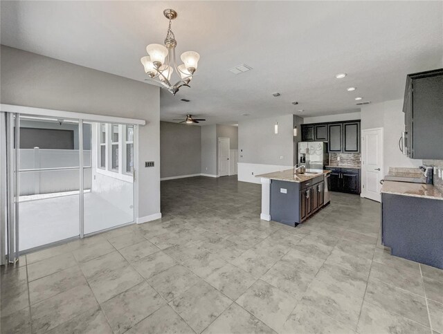 kitchen featuring stainless steel fridge with ice dispenser, an island with sink, decorative light fixtures, decorative backsplash, and ceiling fan with notable chandelier