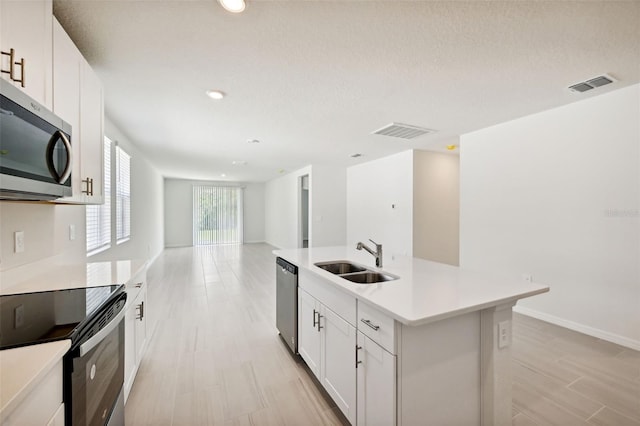 kitchen featuring a kitchen island with sink, stainless steel appliances, a textured ceiling, sink, and white cabinetry