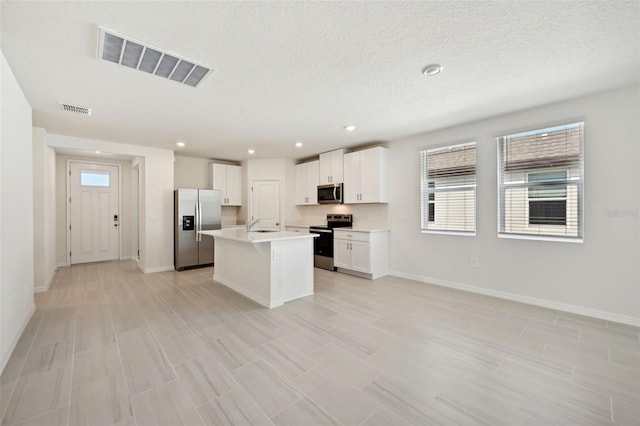 kitchen with stainless steel appliances, sink, white cabinets, a textured ceiling, and a kitchen island with sink