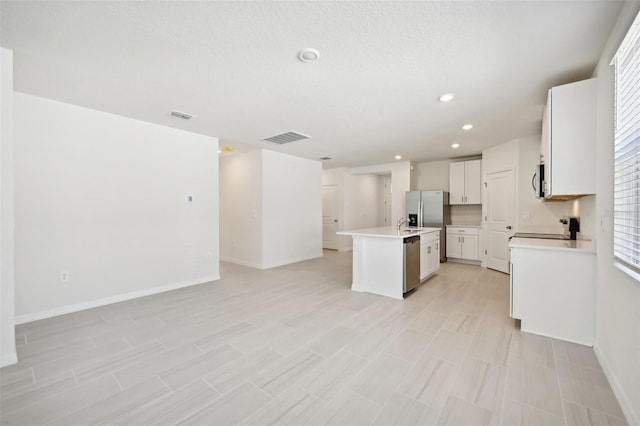 kitchen with an island with sink, a textured ceiling, white cabinets, and stainless steel appliances