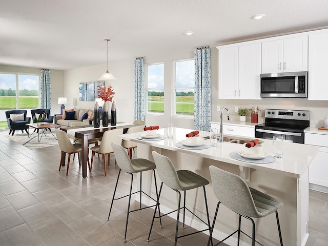 kitchen with pendant lighting, sink, a center island with sink, appliances with stainless steel finishes, and light tile patterned floors