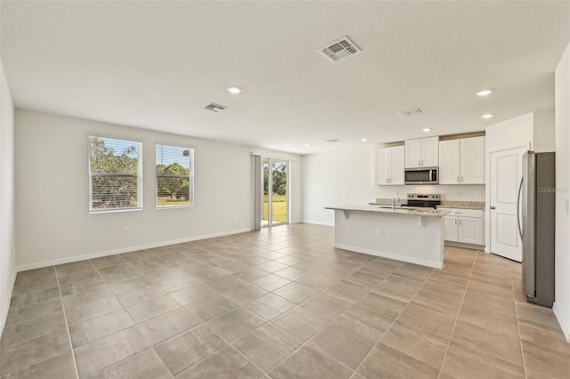 kitchen featuring light stone countertops, stainless steel appliances, an island with sink, a breakfast bar, and white cabinets