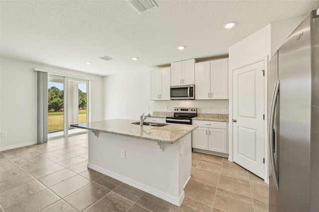 kitchen featuring light stone countertops, an island with sink, white cabinetry, appliances with stainless steel finishes, and sink