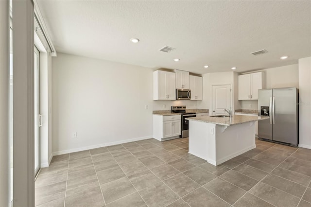 kitchen with light stone countertops, a center island with sink, white cabinetry, appliances with stainless steel finishes, and sink