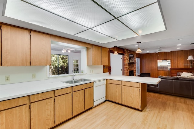 kitchen with sink, a brick fireplace, kitchen peninsula, white dishwasher, and wooden walls