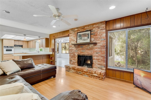 living room featuring wood walls, a textured ceiling, and a brick fireplace