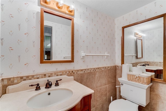 bathroom with a textured ceiling, vanity, toilet, and tile walls