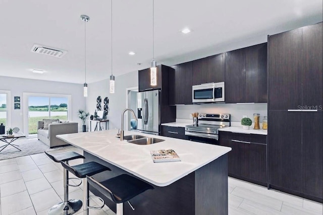 kitchen with appliances with stainless steel finishes, a kitchen breakfast bar, a kitchen island with sink, and decorative light fixtures