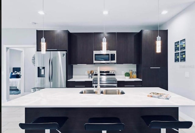 kitchen featuring stainless steel appliances, a kitchen breakfast bar, a kitchen island with sink, and pendant lighting