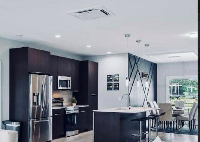 kitchen featuring a center island with sink, stainless steel appliances, hanging light fixtures, a kitchen breakfast bar, and sink