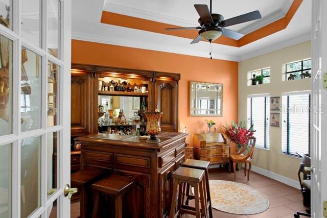 bar with ceiling fan, ornamental molding, light tile patterned floors, and a tray ceiling