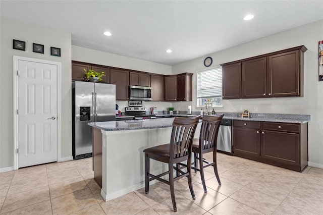 kitchen with a center island, a kitchen bar, appliances with stainless steel finishes, dark brown cabinets, and light stone counters