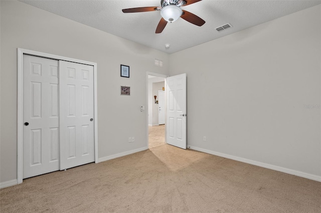 unfurnished bedroom featuring ceiling fan, a closet, light colored carpet, and a textured ceiling