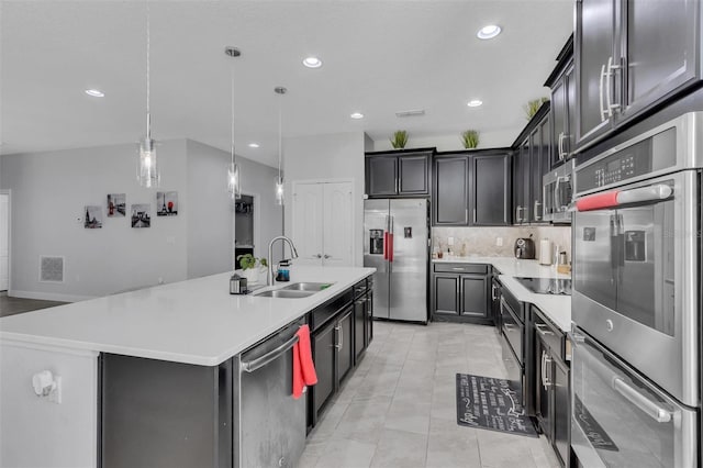 kitchen featuring decorative light fixtures, stainless steel appliances, tasteful backsplash, sink, and a kitchen island with sink