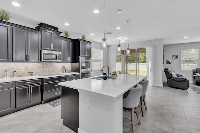 kitchen featuring stainless steel appliances, sink, decorative light fixtures, and an island with sink