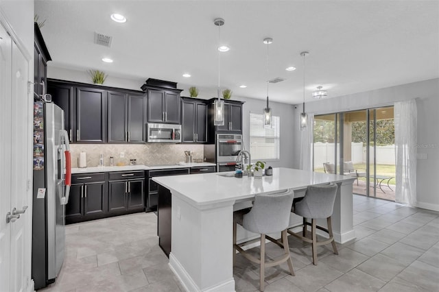 kitchen featuring decorative light fixtures, tasteful backsplash, a kitchen island with sink, appliances with stainless steel finishes, and a breakfast bar area