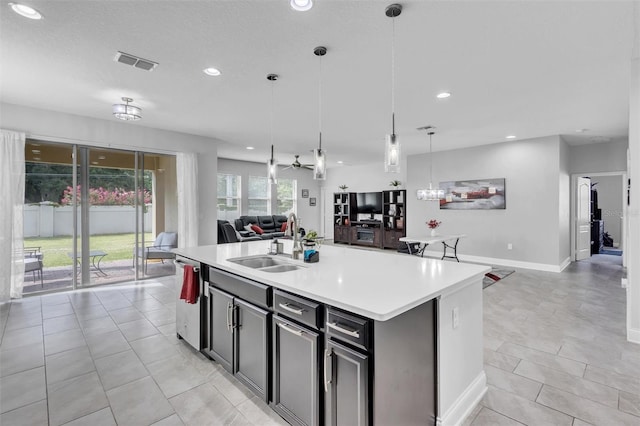 kitchen featuring pendant lighting, sink, light tile patterned flooring, stainless steel dishwasher, and a center island with sink