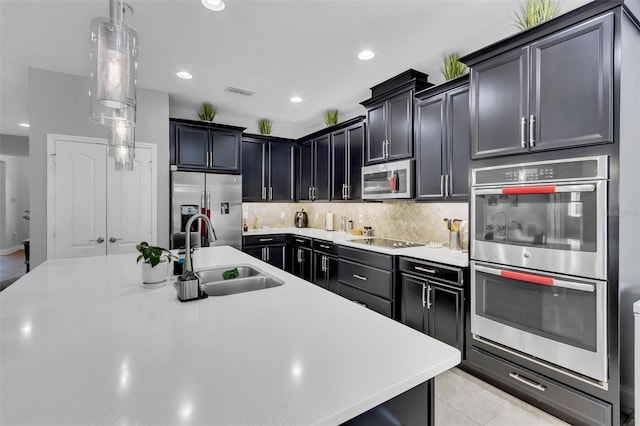 kitchen with pendant lighting, decorative backsplash, sink, an island with sink, and stainless steel appliances