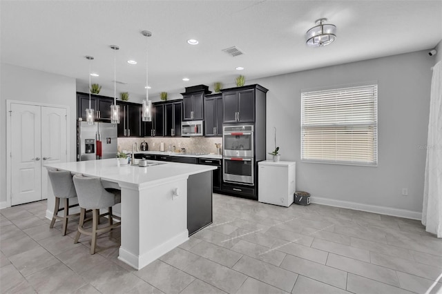 kitchen with sink, hanging light fixtures, appliances with stainless steel finishes, an island with sink, and a kitchen breakfast bar