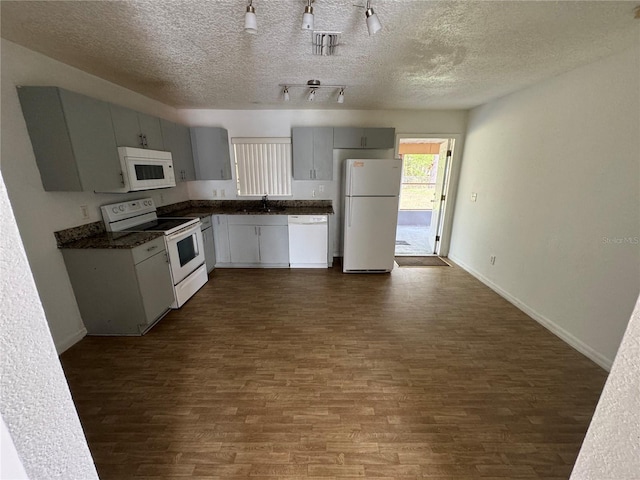 kitchen with dark wood-style floors, dark countertops, a sink, white appliances, and baseboards