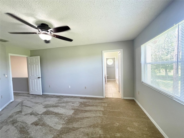 unfurnished bedroom with light carpet, ceiling fan, ensuite bathroom, and a textured ceiling