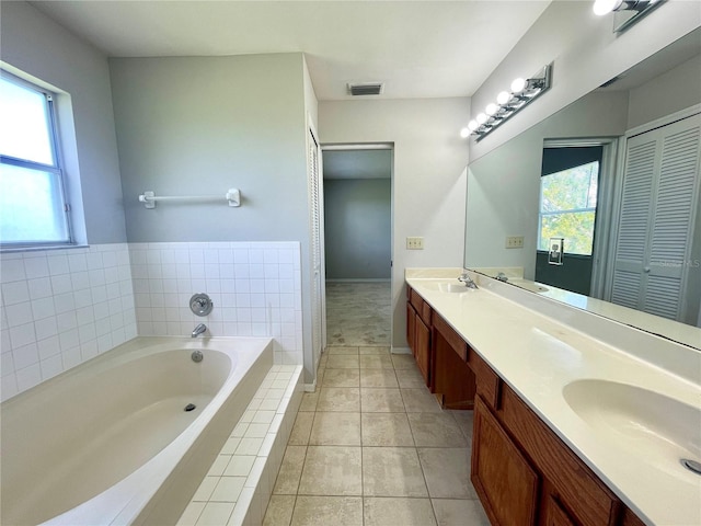 bathroom with tiled bath, a wealth of natural light, tile patterned floors, and vanity