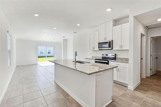 kitchen with light stone counters, appliances with stainless steel finishes, white cabinets, a kitchen island with sink, and a sink