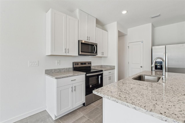 kitchen featuring stainless steel appliances, light tile patterned flooring, white cabinetry, a sink, and light stone countertops