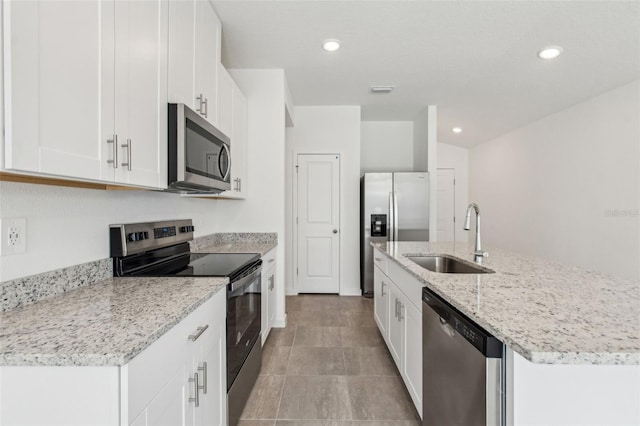 kitchen with white cabinets, an island with sink, light stone counters, stainless steel appliances, and a sink