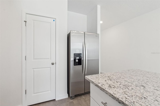 kitchen with light stone counters, stainless steel fridge, and white cabinetry