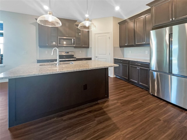 kitchen with pendant lighting, a center island with sink, sink, light stone countertops, and appliances with stainless steel finishes