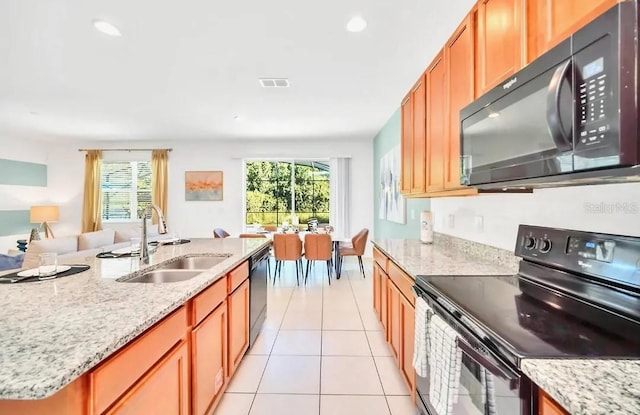 kitchen featuring black appliances, an island with sink, sink, light stone countertops, and light tile patterned floors