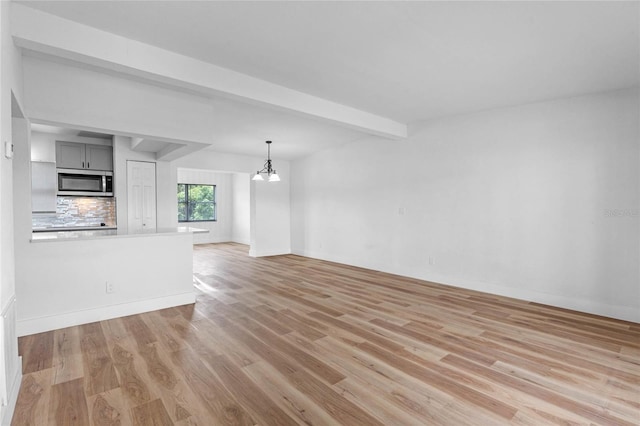 unfurnished living room featuring light wood-type flooring, beam ceiling, and an inviting chandelier