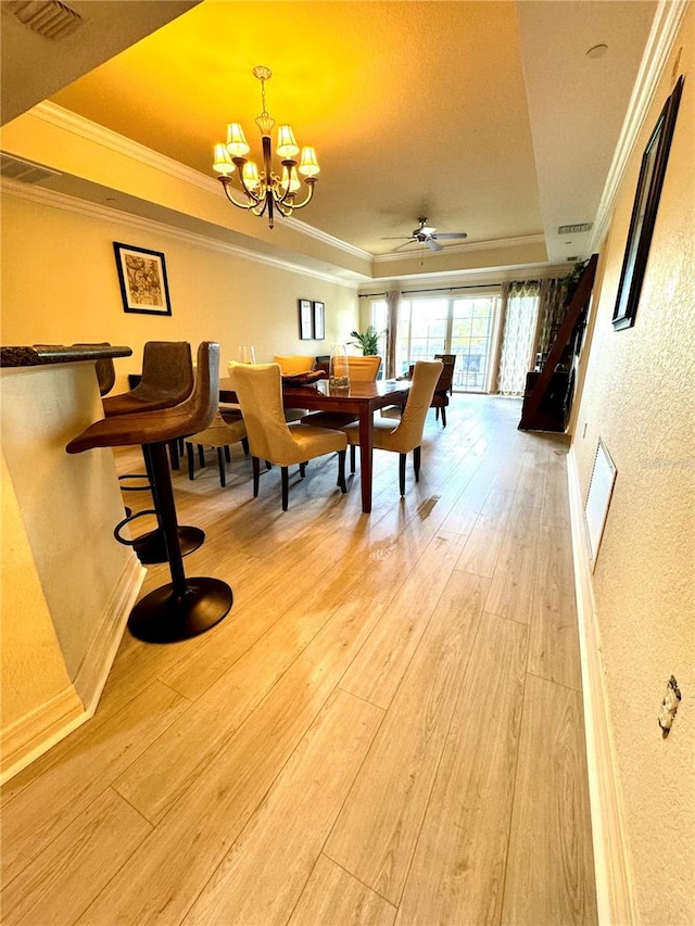 dining area with crown molding, light hardwood / wood-style flooring, and a tray ceiling