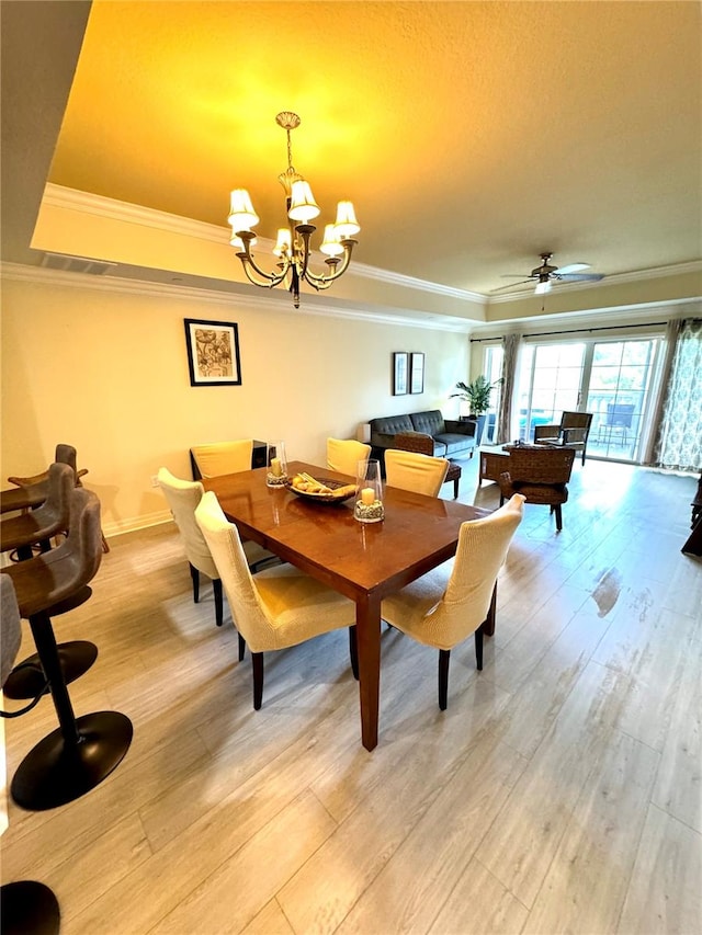 dining room featuring ceiling fan with notable chandelier, light wood-type flooring, a tray ceiling, and ornamental molding