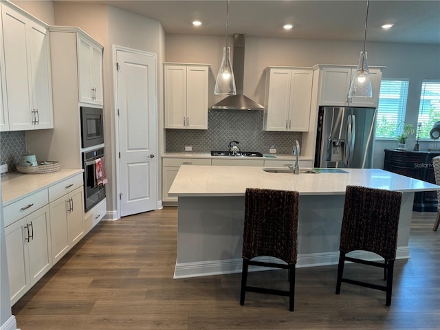 kitchen with appliances with stainless steel finishes, white cabinetry, hanging light fixtures, and wall chimney exhaust hood