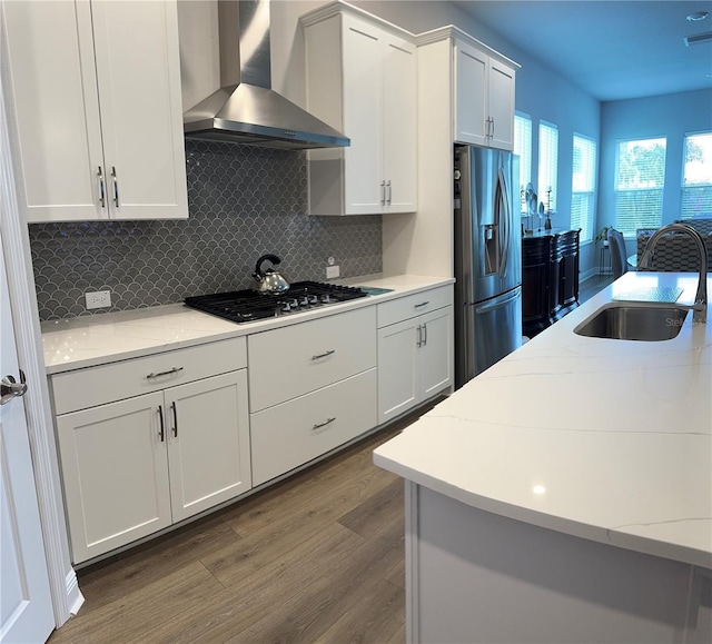 kitchen with light stone countertops, white cabinetry, sink, wall chimney exhaust hood, and stainless steel appliances