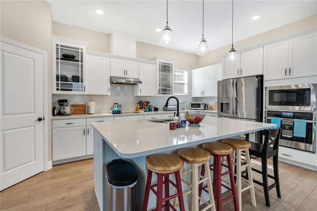 kitchen with pendant lighting, decorative backsplash, an island with sink, white cabinetry, and stainless steel appliances