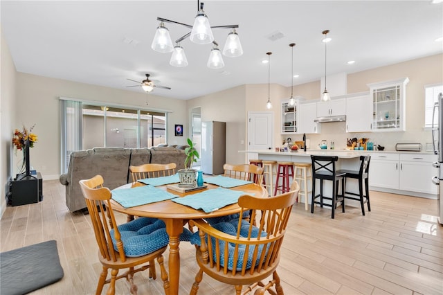 dining room with light hardwood / wood-style floors and ceiling fan with notable chandelier