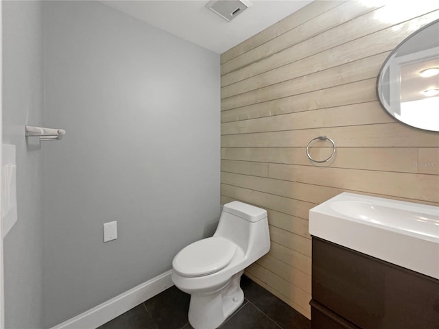 bathroom featuring tile patterned flooring, vanity, toilet, and wooden walls