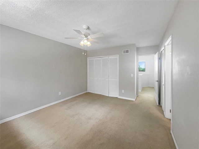 unfurnished bedroom featuring ceiling fan, a closet, light carpet, and a textured ceiling