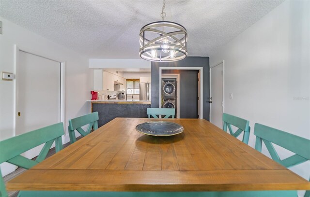 dining room featuring a textured ceiling, a chandelier, stacked washer / drying machine, and sink