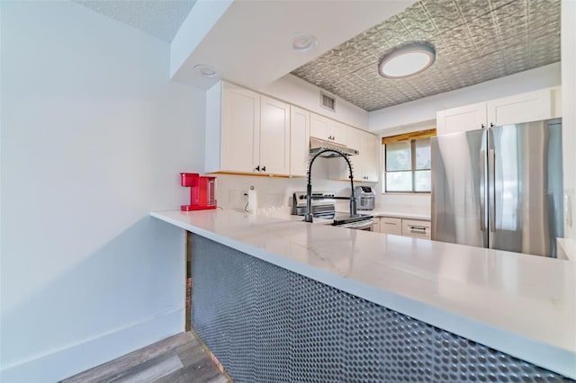 kitchen with appliances with stainless steel finishes, white cabinetry, hardwood / wood-style floors, and kitchen peninsula